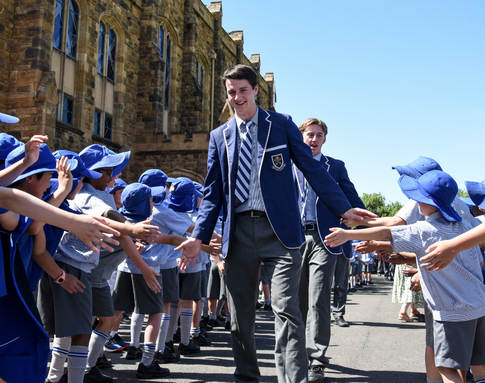 Student walking down avenue of honor high-fiving junior school students